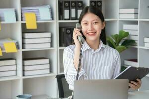asiatisch Geschäftsfrau reden auf das Telefon Arbeiten im modern Büro Plaudern mit Kunden zum ein Neu Weg von tun Geschäft im das Büro. foto