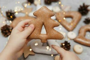 Kinder- Hände halt ein Lebkuchen im das gestalten von ein Weihnachten Baum. das Konzept von Weihnachten Süßigkeiten, Spielzeuge, Girlanden und Bokeh. Dekor zum Neu Jahr Feiertage. foto