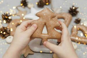 Kinder- Hände halt ein Lebkuchen im das gestalten von ein Weihnachten Baum. das Konzept von Weihnachten Süßigkeiten, Spielzeuge, Girlanden und Bokeh. Dekor zum Neu Jahr Feiertage. foto