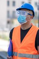 Bauarbeiter mit blauem Schutzhelm, Warnweste und chirurgischer Schutzmaske foto