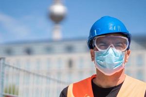 Bauarbeiter mit blauem Schutzhelm, Warnweste und chirurgischer Schutzmaske