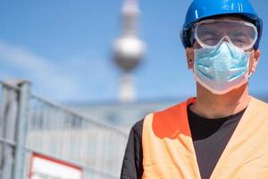 Bauarbeiter mit blauem Schutzhelm, Warnweste und chirurgischer Schutzmaske