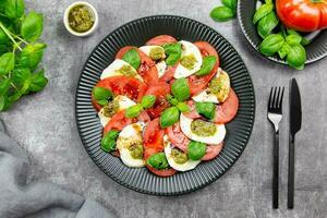 traditionell Italienisch Caprese Salat mit geschnitten Tomaten, Mozzarella, Basilikum, Pesto Soße und würzen auf ein dunkel grau Beton Hintergrund. oben Sicht. foto