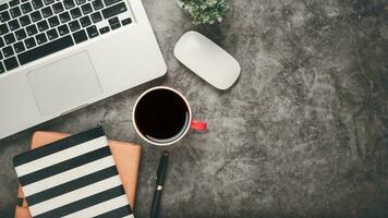 dunkel Büro Schreibtisch Arbeitsplatz mit Laptop, Notizbuch, Maus, Stift und Tasse von Kaffee, oben Aussicht eben legen mit Kopieren Raum. foto