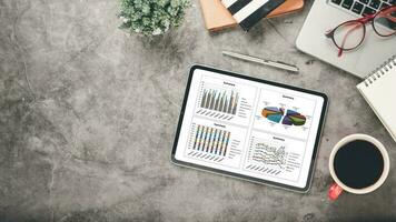 tablet mit diagrammen und berichten über den schreibtischarbeitsplatz. Draufsicht flach liegen foto