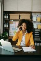 Geschäft afrikanisch Frau reden auf das Telefon und mit ein Laptop mit ein Lächeln während Sitzung beim Büro foto