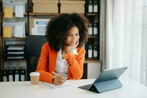 jung afrikanisch Frau Tippen auf Tablette und Laptop während Sitzung beim das Arbeiten hölzern Tabelle modern Büro foto