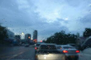 verschwommen Aussicht von Auto auf Straße durch nass Windschutzscheibe mit Regen Tropfen Hintergrund. foto
