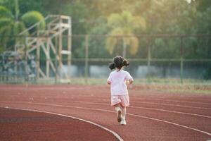 zurück Seite. Baby asiatisch Mädchen Lauf Joggen beim Laufen Schiene, Feld beim Stadion. wenig Mädchen Laufen Sonnenuntergang glücklich Baby Mädchen lächelnd. wenig Mädchen Laufen beim Sonnenuntergang. süß Baby Mädchen Laufen beim Laufen Schiene. foto