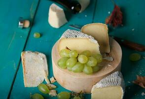 Käse, Trauben und Wein auf hölzern cyan Oberfläche. foto