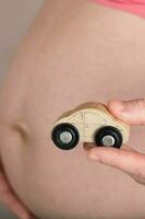jung schwanger Frau hält klein hölzern Fahrzeug. foto