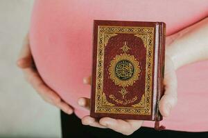 jung schwanger Frau hält Stechpalme Buch von Koran. foto