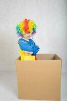 Junge von fünf Jahre gekleidet im das Kostüm von ein Clown bleibt im ein Karton Papier Kasten. foto