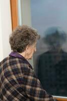 alt Frau von 80 Jahre alt bleibt schließen zu das Fenster foto