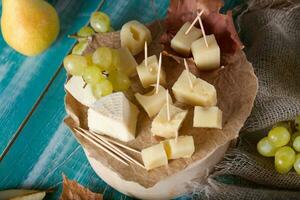 Käse Scheiben, Birne, und Trauben auf ein hölzern Stand. foto