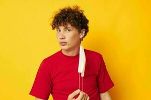 Kerl mit rot lockig Haar im ein rot T-Shirt medizinisch Maske Schutz Lebensstil unverändert foto