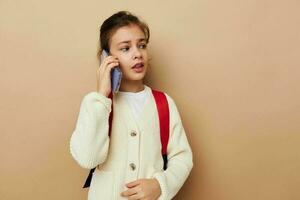 Porträt von glücklich lächelnd Kind Mädchen reden auf das Telefon mit ein Rucksack Beige Hintergrund foto