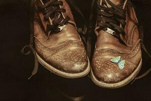 ein Paar von braun Jahrgang Leder Schuhe mit ein Schmetterling Brosche auf ein dunkel Hintergrund. schön Leder Schuhe. retro Schuhe. foto
