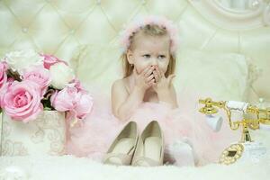 Zwei Jahre alt Kind. traurig wenig Mädchen im ein Clever Rosa Kleid mit ein retro Telefon und Mamas Schuhe. foto