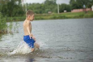 ein wenig Junge läuft in ein kalt Fluss. das Kind schwimmt im das See im Sommer. foto