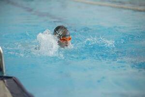 ein Junge im ein Schwimmen Deckel und Brille ist Schwimmen im das Sport Schwimmbad. foto