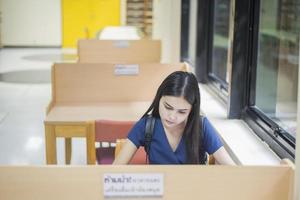 attraktives weibliches asiatisches Universitätsstudenten-Lesebuch in der Bibliothek foto