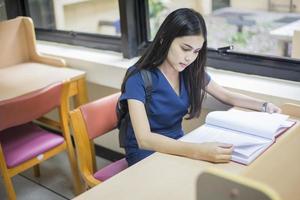 attraktives weibliches asiatisches Universitätsstudenten-Lesebuch in der Bibliothek foto
