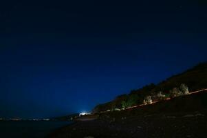 Nacht Landschaft. Aussicht von das Nacht Stadt in der Nähe von das Meer Küste foto