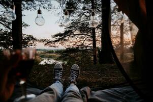 ein Nahansicht Foto von das Intentionen von Damen Beine. das Mädchen hat ein Glas von Wein oder Wasser im ihr Hände. das Konzept von ein Tourist Trekking Expedition. Aussicht von das Zelt zu das Landschaft