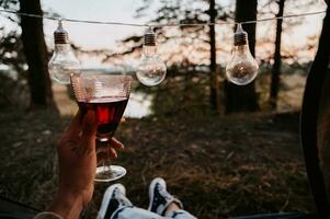 ein Nahansicht Foto von das Intentionen von Damen Beine. das Mädchen hat ein Glas von Wein oder Wasser im ihr Hände. das Konzept von ein Tourist Trekking Expedition. Aussicht von das Zelt zu das Landschaft