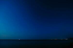 Nacht Landschaft. Aussicht von das sternenklar Himmel und das Nacht Stadt durch das Meer Küste foto