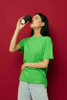 charmant jung asiatisch Frau Lächeln Grün T-Shirt schwarz Einweg Tassen Mode Studio Modell- unverändert foto