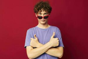 Porträt von ein jung lockig Mann Kerl im ein lila T-Shirt mit Sonnenbrille posieren Jugend Stil foto