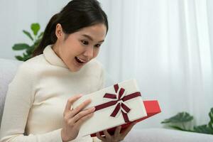 hübsche asiatische frau fühlt sich überrascht und sieht interesse in der geschenkbox aus. süßes Mädchen aufgeregt offene Geschenkbox. geburtstag, feier, weihnachten, neujahrsfest, danken, feiern, valentinstag, jahrestag foto