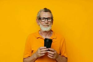 Senior grauhaarig Mann im ein Gelb T-Shirt ein Glas mit ein trinken unverändert foto