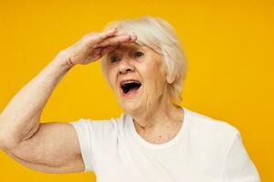 Porträt von ein alt freundlich Frau im beiläufig T-Shirt Gesten mit seine Hände abgeschnitten Aussicht foto