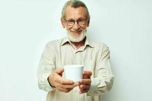 alt Mann mit Brille zeigt an ein Becher auf ein Weiß Hintergrund foto
