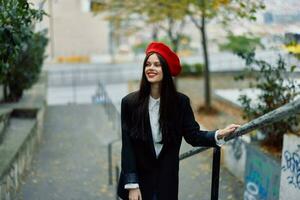 Mode Frau Gehen Nieder Schritte gegen Stadt Hintergrund im stilvoll Kleider mit rot Lippen und rot Baskenmütze, reisen, filmisch Farbe, retro Jahrgang Stil, städtisch Mode Lebensstil. foto