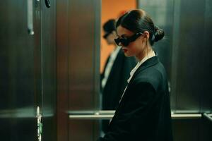 stilvoll Frau im schwarz Jacke und Sonnenbrille posieren im Aufzug, Mode Modell, dunkel filmisch Licht und Farbe, Glanz Jahrgang foto