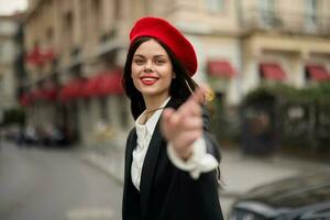 Mode Frau Lächeln mit Zähne Stehen auf das Straße im Vorderseite von das Stadt Tourist Folgen mich stilvoll Kleider mit rot Lippen und rot Baskenmütze, reisen, filmisch Farbe, retro Jahrgang Stil, städtisch Mode. foto