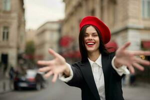 Mode Frau Lächeln mit Zähne Stehen auf das Straße im Vorderseite von das Stadt Tourist Folgen mich stilvoll Kleider mit rot Lippen und rot Baskenmütze, reisen, filmisch Farbe, retro Jahrgang Stil, städtisch Mode. foto