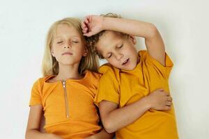 Junge und Mädchen Lüge auf ein Weiß Hintergrund im Gelb T-Shirts Emotionen foto
