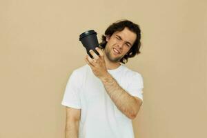 heiter Mann im ein Weiß T-Shirt mit ein schwarz Glas im Hand Beige Hintergrund foto