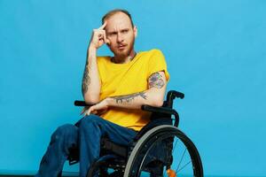 ein Mann sitzt im ein Rollstuhl Nachdenklichkeit im ein T-Shirt auf ein Blau Hintergrund im das Studio, das Konzept von ein kostenlos barrierefrei Umgebung zum Menschen mit Behinderungen foto