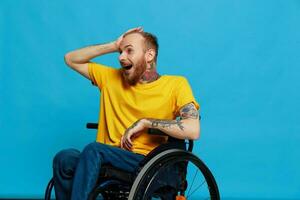 ein Mann im ein Rollstuhl überrascht und öffnen Mund im ein T-Shirt mit Tätowierungen auf seine Waffen sitzt auf ein Blau Studio Hintergrund, ein voll Leben, ein echt Person foto