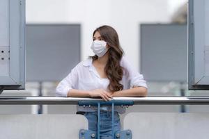 Porträt der jungen Frau mit dem Smileygesicht, das Gesichtsmaskenschutzspaziergänge in einer Stadt trägt foto