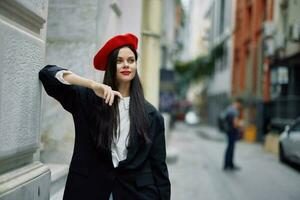 Frau Stehen in der Nähe von ein Mauer im das Stadt tragen ein stilvoll Jacke und rot Baskenmütze mit rot Lippen, Reise und Freizeit, Französisch Stil von Kleid. foto