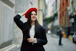 Frau Stehen in der Nähe von ein Mauer im das Stadt tragen ein stilvoll Jacke und rot Baskenmütze mit rot Lippen, Reise und Freizeit, Französisch Stil von Kleid. foto