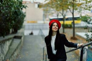 Mode Frau Gehen Nieder Schritte gegen Stadt Hintergrund im stilvoll Kleider mit rot Lippen und rot Baskenmütze, reisen, filmisch Farbe, retro Jahrgang Stil, städtisch Mode Lebensstil. foto