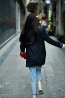 Mode Frau Tourist im stilvoll Kleider im ein Jacke und rot Baskenmütze Laufen Nieder das eng Straße von das Stadt Lächeln und Glück Reise, Französisch Stil, filmisch Farbe. foto